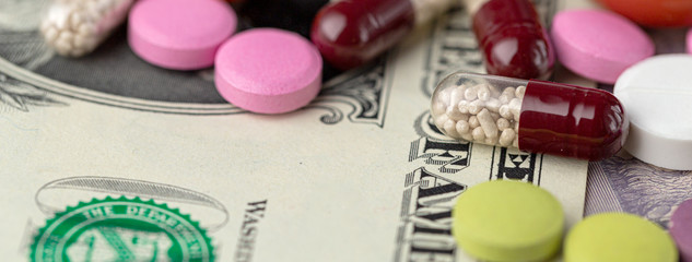 The concept of making money on medicines. Multicolored drugs on a background of dollars. Different remedy, pills, capsule, antibiotic and vitamin, panoramic banner.