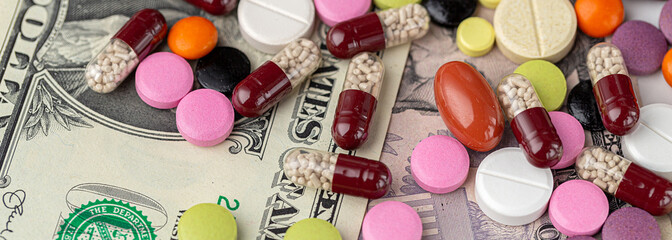 The concept of making money on medicines. Multicolored drugs on a background of dollars. Different remedy, pills, capsule, antibiotic and vitamin, panoramic banner.