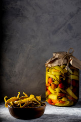 pickled spicy green and red pepper in an jar on a gray background and a wooden bowl with pepper pods, closeup