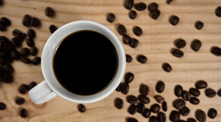 Black coffee in white cup vertically from above on board with coffee beans, intentionally blurred