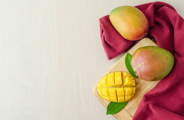 top view ripe juicy mango with leaves on white and red background. slice and several whole exotic fruit on wooden board. copy space, soft focus