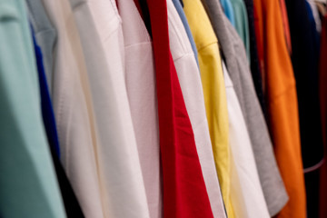 Row of colorful t-shirts on shoulders hangers in retail shop