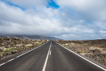 Endless road to Timanfaya National park in Lanzarote, Canary Ispands, Spain, Europe, Africa. Volcanic, black sand, harsh, tough, inhospitable, dry, sub-tropical, desert landscape.