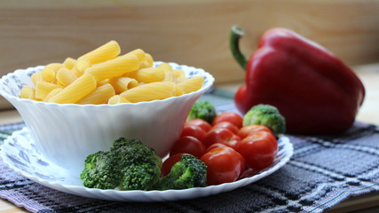 pasta in a white bowl with cherry tomatoes and broccoli on a background of large red pepper