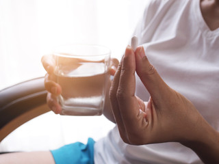 Close up white pill tablet on hand and glass of water to take medicine to cure illness.