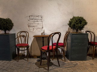 vintage empty table and chairs in the darkness near the trees in wooden boxes on the background of a gray white ragged wall