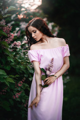 Beautiful young girl in a pink dress posing in flowers. Posing and enjoying the spring. Art work of romantic woman .Pretty tenderness model looking at camera. Gardening..