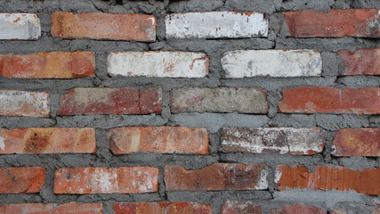 bricks of different colors with rough gray concrete seams in the structure of an old wall