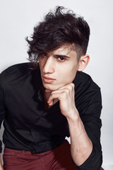 Young guy in a black shirt similar to Adriano Celentano posing on a white background. Fashion portrait