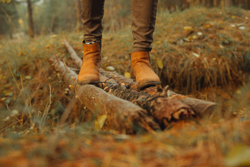 An unreliable rickety bridge over a pit of pine logs. Crossing the moat in the forest. A woman crosses a dangerous bridge. Feet in boots close-up.