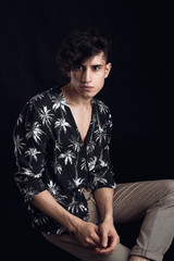Young guy in a black shirt similar to Adriano Celentano posing on a black background. Fashion portrait