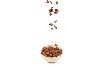 Chocolate corn flakes falling to the white bowl isolated on white. Motion.