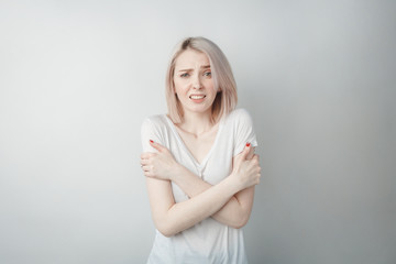 Portrait of a young girl in a white T-shirt on a white background, crossed her arms over her chest, froze