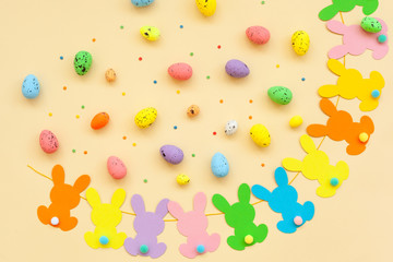 Colorful Easter eggs and handmade bunny easter garland on beige background. Top view, flat lay.
