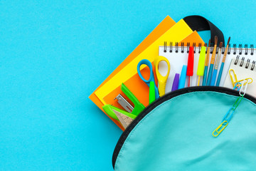 Concept back to school. Full turquoise School Backpack with supplies on blue background. FLat lay.