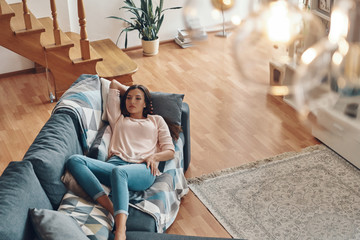 Obraz premium Top view of relaxed young woman in casual clothing resting on sofa while spending time at home