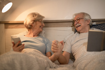 Obraz premium Happy mature couple holding hands while communicating in bed in the evening.