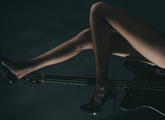 Virtuoso, art of sex, sensual music. Guitar and female legs on a black background. Beautiful composition for design. Shop of musical instruments, advertising guitar. Tights in box and musical strings