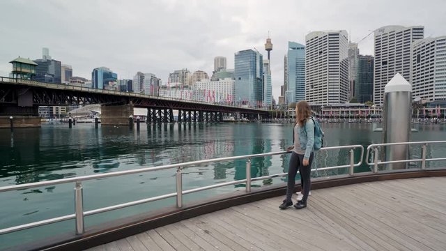 Tracking shot of African American man and Caucasian woman holding hands and walking along the pier at Darling Harbour, Sydney