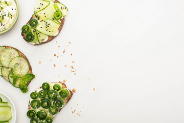 top view of fresh cucumber toasts with seeds, basil leaves near yogurt in bowl on white background