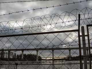 Fence with barbed wire rings on the river Bank near the bridge on a spring day