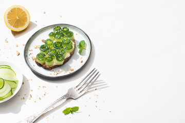 fresh cucumber toast with sesame and mint leaves on plate near fork and lemon on white background
