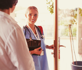 Female doctor with clipboard during home visit while entering house