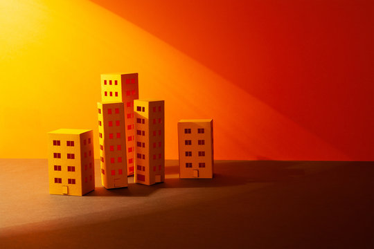 Miniature city evening time sunset landscape. Abstract yellow paper houses urban architecture wallpaper. Simplified town layout high-rise buildings skyscrapers, many windows. Orange yellow background