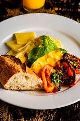 Breakfast plate with scrambled eggs, cheddar cheese, fresh basil, grilled tomatoes and crispy baguette. Classic traditional American Restaurant breakfast or brunch favorite. 