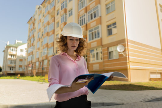 Focused female enginner in hardhat reading document on street