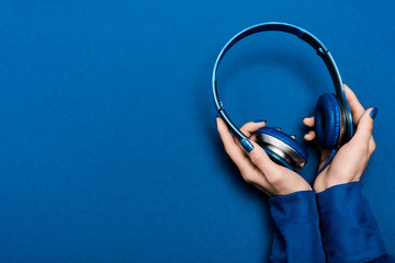 cropped view of woman holding headphones on blue background
