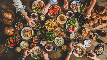 Photo sur Aluminium Manger Turkish breakfast. Flat-lay of family eating pastry, vegetables, greens, cheeses, fried eggs, jams from oriental tableware, tea in copper pot and tulip glasses over rustic wooden background, top view