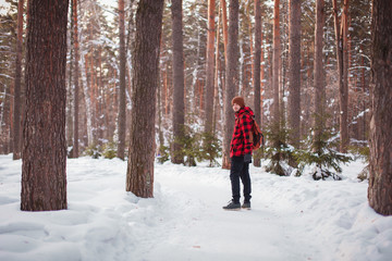 Male tourist with backpack walks on snow pine forest. Guy hiking at nature. Concept of winter holiday or vacation..