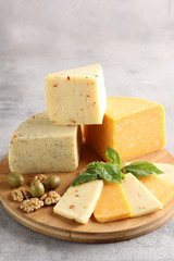 Assortment of cheeses. Sliced cheese on a wooden board with olives, nuts and mint on a light grey background. Background image, copy space