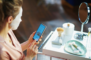 woman with facial mask with smartphone buying cosmetics