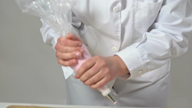 A female baker squeezes cream from a cone for baking marshmallows and meringues and makarons, In white uniform.
