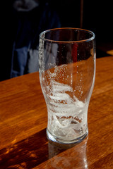 Empty beer glass standing on a table at the pub, lit by the sun from the window.