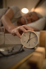 Close-up of mature man turning off ringing alarm clock on bedside table.