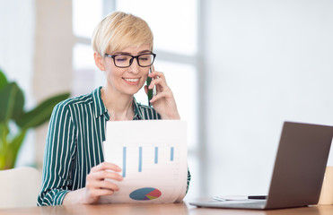 Happy Businesswoman Talking On Phone Holding Charts Sitting In Office