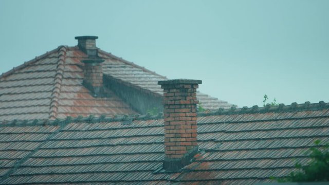 Heavy Summer Storm Raining Over a contryside tile rooftop and chimney