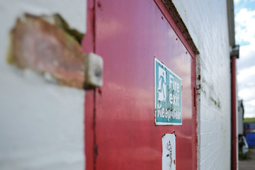 Shallow focus of an old Fire Exit and No Smoking sign seen attached for a fire door, used for emergency exit for a warehouse and logistics company.