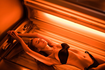 Young beautiful woman lying on a tanning bed at health spa - obrazy, fototapety, plakaty
