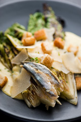 Caesar Salad. Grilled Romaine lettuce leaves topped with classic Caesar salad dressing and garnished with butter garlic croutons shaved parmesan cheese and whole anchovies. Classic American Salad.