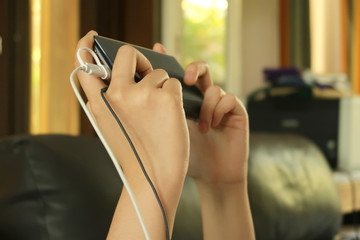 Someone hands is holding a mobile phone which has a power charging wire and black wire of ear phone.