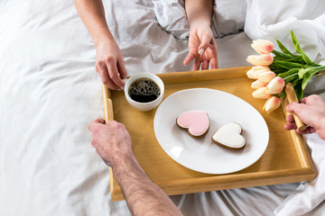 Coffee in bed. Male hands hold out a serving tray.  Two gingerbread cookies on a white plate. 