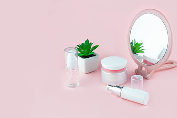 Cosmetic bottles with serum, gel, face cream on a pink background with a flower and a mirror. Skin cosmetics, minimalism