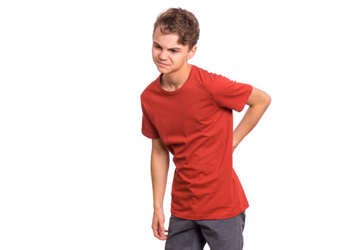 Portrait of unhappy teen boy suffering from backache, isolated on white background. Cute young teenager hands touching back pain. Upset child massaging his back suffering from discomfort ache pain.