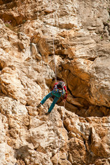 climber descends rappelling, by mountaineering rope, rock wall background