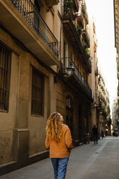 Fototapeta Girl walking through the streets in Barcelona. Cute girl with blond curly hair walking through the streets on Barcelona looking at the buildings and doing tourism