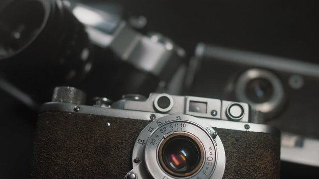 Vintage film photo camera lies in background of other old analog cameras, smooth cinematic motion. Chrome surface reflects light, close up.